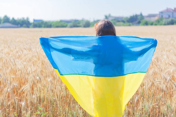 dívka s vlajkou Ukrajiny v pšeničném poli zpětný pohled. Koncept národní ukrajinské dovolené. Den nezávislosti Ukrajiny. - Fotografie, Obrázek