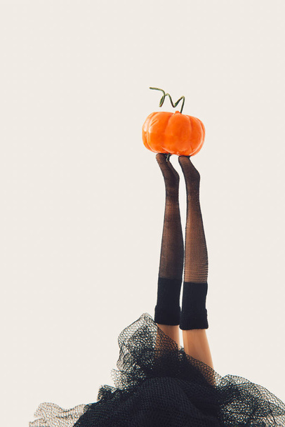 Mädchen Puppe Hexe spielen mit orangefarbenen Kürbis vor hellem Hintergrund. Minimale Nahaufnahme halloween Konzept. Kreative Spaß-Horror-Idee. - Foto, Bild