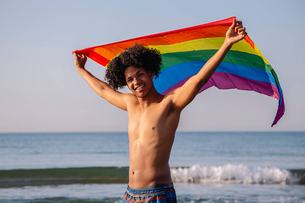 Jeune homme latino avec des cheveux afro montrant drapeau lgtbi - Photo, image