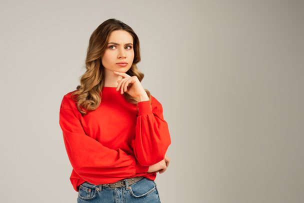 pensive woman in red sweatshirt looking away and thinking isolated on grey - Photo, Image