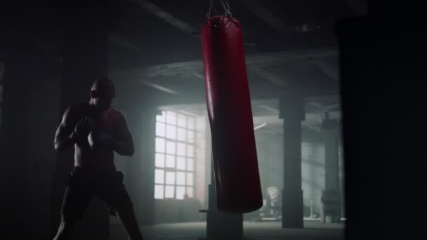 A sportoló kesztyűben üti a bokszzsákot. Egy férfi, aki sporttáskára gyúr.  - Felvétel, videó