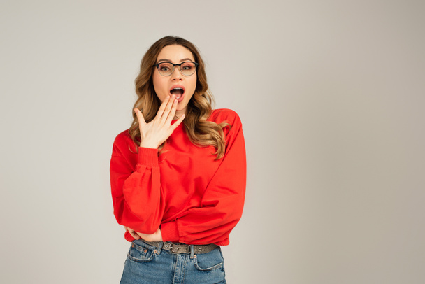 shocked woman in sweatshirt and eyeglasses with open mouth isolated on grey - 写真・画像