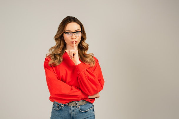 curly woman in eyeglasses showing shh sign isolated on grey - Foto, afbeelding