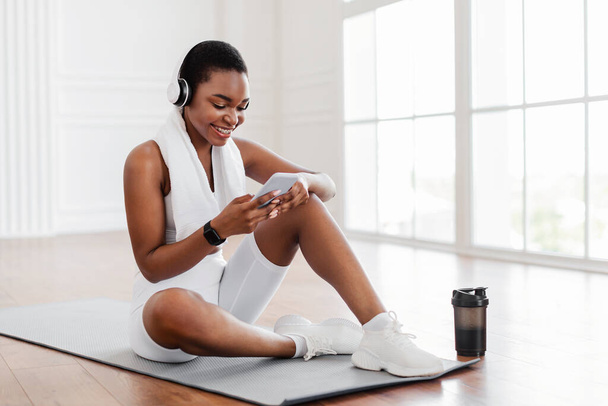 Fitness μαύρη κυρία ακούγοντας μουσική χρησιμοποιώντας το τηλέφωνο κατά τη διάρκεια του διαλείμματος - Φωτογραφία, εικόνα