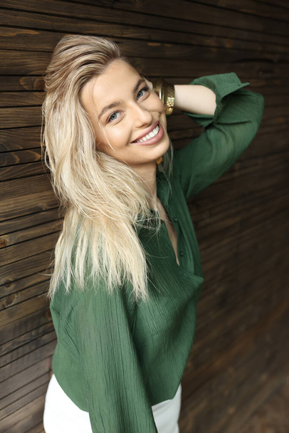 girl standing on a background of a wooden wall and smiling. She is wearing a green shirt - Foto, immagini