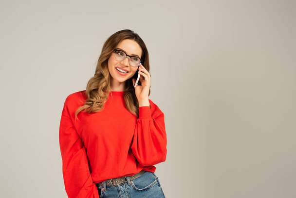 joyful woman in eyeglasses talking on smartphone isolated on grey - Fotó, kép