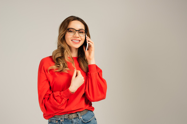joyful woman in eyeglasses talking on cellphone isolated on grey - Foto, imagen