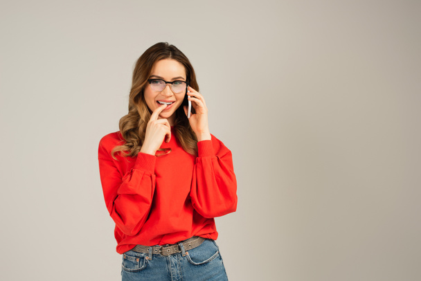 Χαμογελαστή γυναίκα με γυαλιά που μιλάει στο κινητό απομονωμένη στο γκρι. - Φωτογραφία, εικόνα