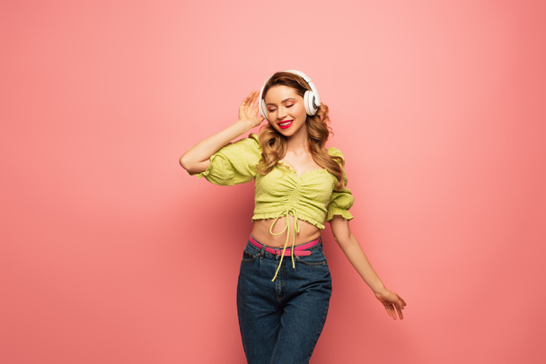 positive  woman adjusting wireless headphones on pink - Valokuva, kuva