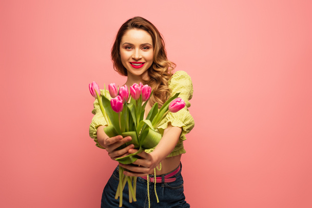pleased woman holding bouquet of blurred flowers isolated on pink - Fotoğraf, Görsel