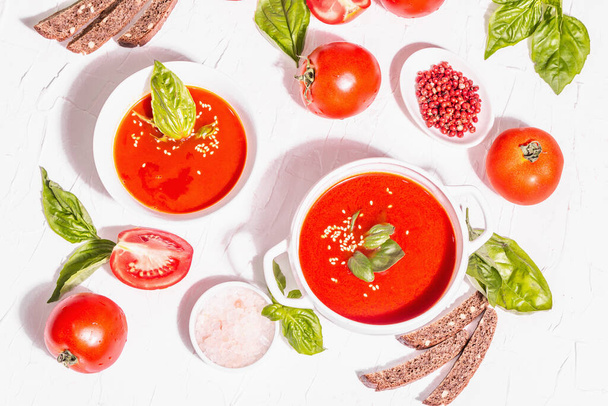 Bowls with homemade tomato soup. Ripe vegetables, fresh basil leaves, breadsticks, aromatic spices. Trendy hard light, dark shadow. White putty background, top view - Fotoğraf, Görsel