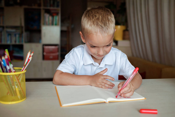 Gelukkige linkshandige jongen schrijft in het papieren boek met zijn linkerhand, internationale linkshandige dag - Foto, afbeelding