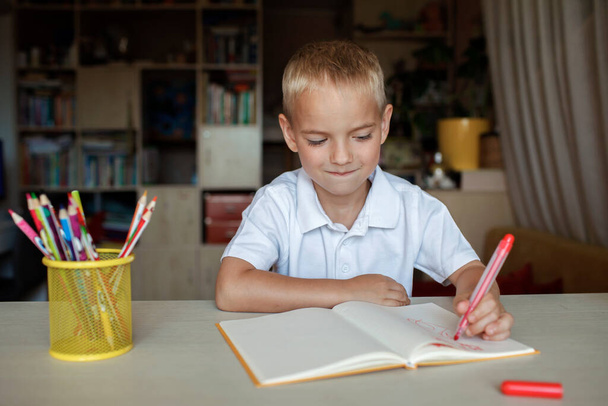 Gelukkige linkshandige jongen schrijft in het papieren boek met zijn linkerhand, internationale linkshandige dag - Foto, afbeelding
