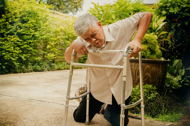 Aîné homme asiatique qui est en mauvaise santé avec la dystrophie mucculaire, la polyarthrite rhumatoïde et l'ostéoporose, glisse sur le blanc en utilisant un, aide à la marche en essayant de s'aider : Concept d'assurance maladie - Photo, image