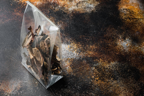 Mezcla de champiñones secos silvestres picados, sobre fondo rústico oscuro viejo, en paquete de plástico, con espacio para copyspace texto - Foto, Imagen