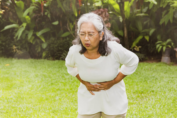 消化管の痛み、腹部の痛みに苦しんでいる高齢のアジアの女性は、手で胃に触れることによって拷問:退職した女性は健康上の問題と健康保険を持っています. - 写真・画像