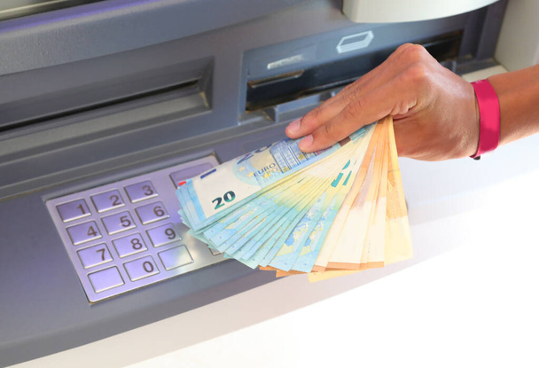billetes en euros que acaban de retirarse del cajero automático y de la mano que los recoge con el teclado numérico para introducir el PIN - Foto, imagen