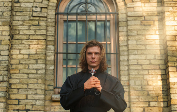 Χριστιανός ιερέας με σταυρό στέκεται δίπλα στην εκκλησία. - Φωτογραφία, εικόνα
