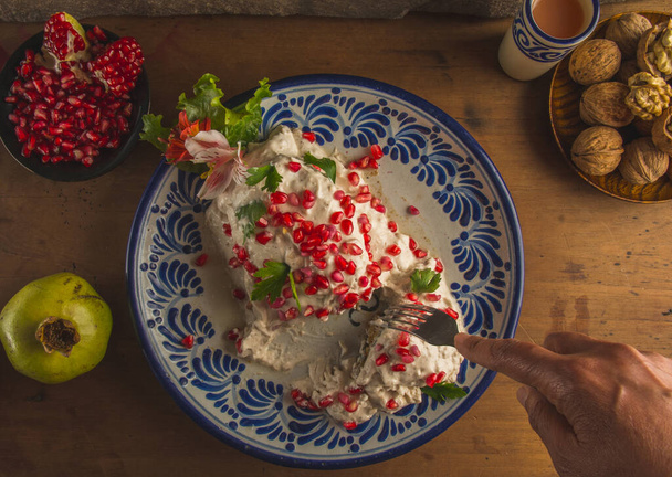 Chiles en Nogada, una ricetta messicana al 100% con i suoi ingredienti principali su un lato, come la noce, gradana, servita su un piatto Puebla talavera, su un tavolo di legno, il ripieno si distingue. - Foto, immagini