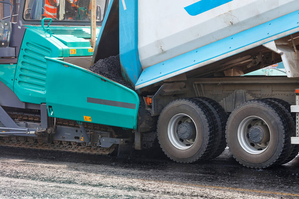 Um caminhão de descarga de asfalto de seu corpo em um pavimentador de asfalto em um canteiro de obras. Close-up, espaço de cópia. - Foto, Imagem