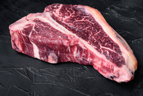 Száraz érlelésű nyers T-bone vagy porterhouse marhahús márványozott hús elsődleges steak készlet, fekete kő alapon - Fotó, kép