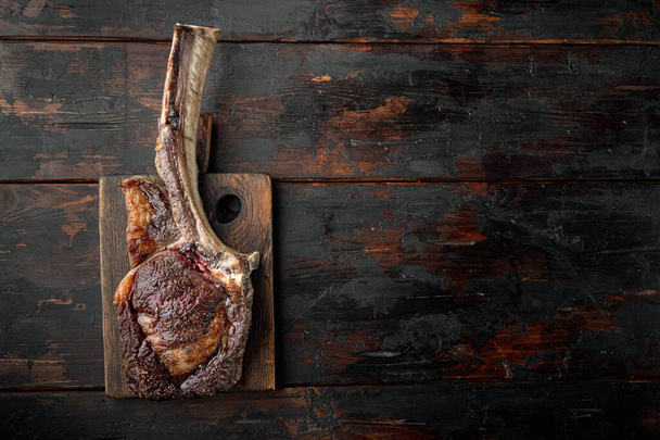 Steak on the bone. tomahawk steak freshly grilled dry aged BBQ food set, on wooden serving board, on old dark  wooden table background, top view flat lay, with copy space for text - Photo, Image