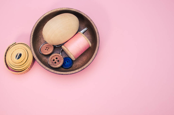A small wooden bowl with sewing supplies on a pink background - Fotó, kép