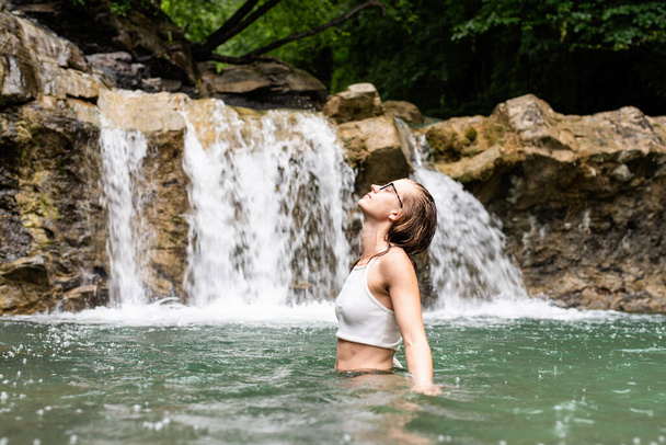 Тропическая природа и отдых. Женщина плавает в горной реке с водопадом - Фото, изображение
