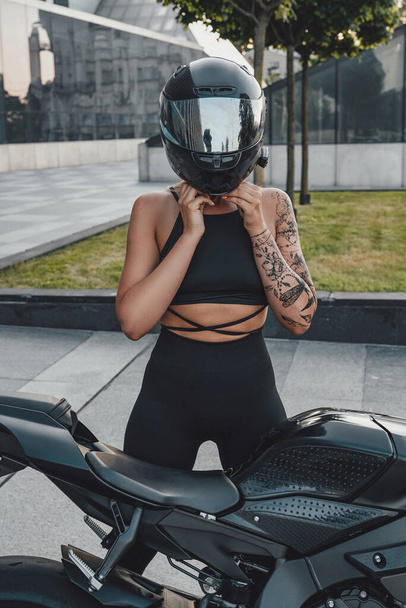 Miğfer takan ve siyah motosikletli spor giyimli bir kadın. - Fotoğraf, Görsel