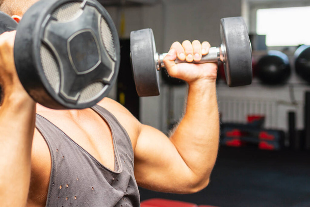 Young fit man in a gym exercising with dumbbells.healthy man working out with dumbbells.closeup. - 写真・画像