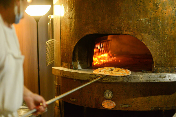 MIGNANO PC, ITALY - Jul 10, 2021: A chef preparing pizza in a traditional and classic copper oven in Mignano, Italy - Foto, imagen
