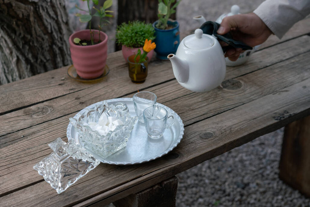 Het gieten van traditionele Iraanse thee. Witte theepot, kristalsuiker, bord op een houten tafel buiten. Shiraz, Iran. - Foto, afbeelding
