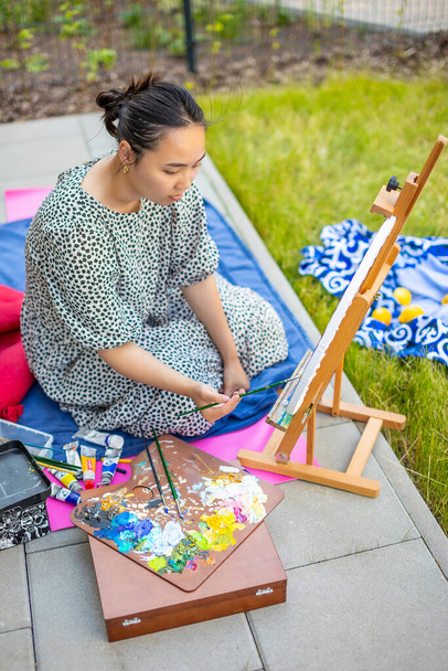 Азиатская молодая женщина рисует картину на домашней террасе - Фото, изображение