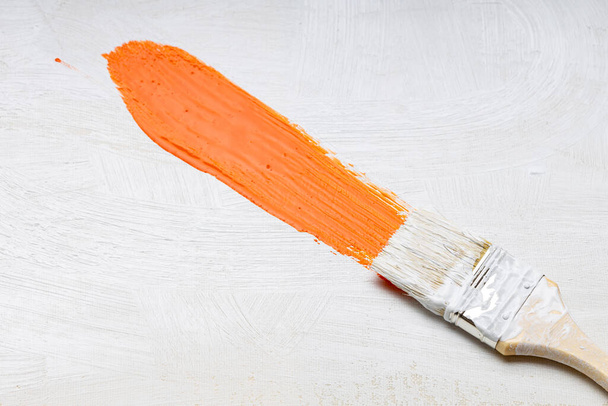 un pincel con cerdas blancas deja un rastro naranja de pintura, un pincel de pintor y un lienzo - Foto, Imagen