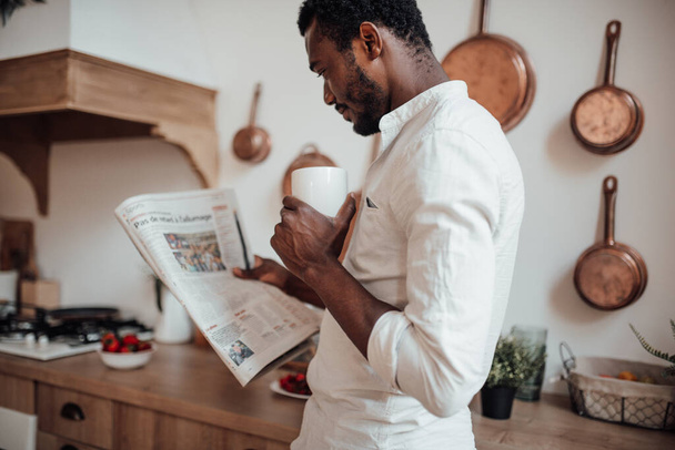 african american man in shirt reading newspaper and drinking coffee - Foto, imagen