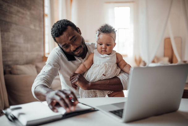 businessman working from home on laptop while holding daughter - Photo, Image