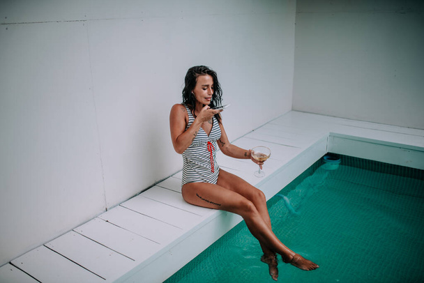 mujer joven con smartphone y cóctel cerca de la piscina - Foto, imagen