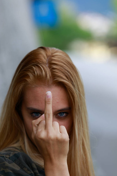 Insolente mulher jovem rude dando um gesto obsceno com o dedo médio como ela olha para a câmera com foco em sua mão em close-up - Foto, Imagem