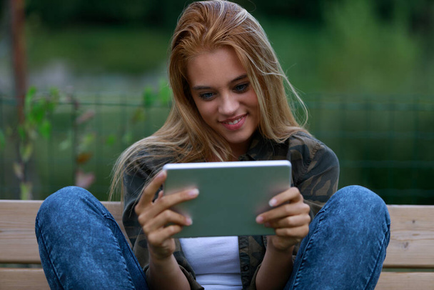 junge Frau sitzt informell auf einer Bank und genießt digitale Inhalte, vielleicht in sozialen Netzwerken, beim Surfen im Internet oder bei Videos - Foto, Bild