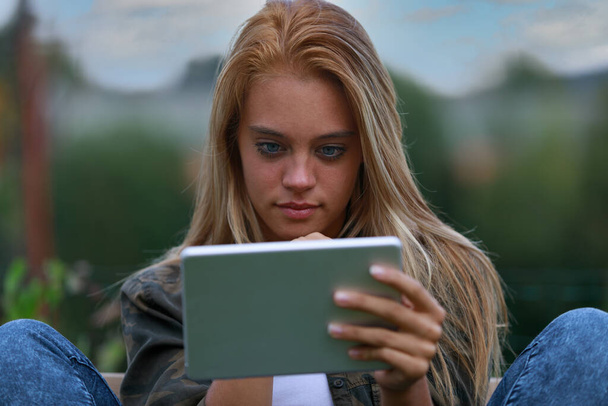 giovane donna seduta informalmente su una panchina mentre si gode i contenuti digitali, magari nei social network, navigando in internet o nei video - Foto, immagini