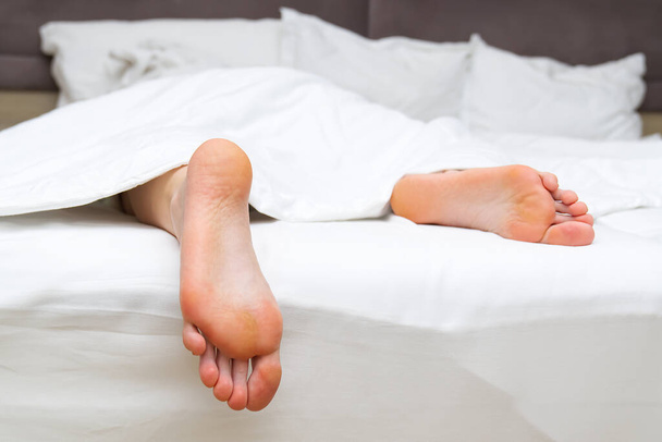 clean adult feet in bed with white linen - Valokuva, kuva