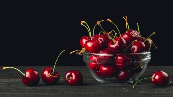 Cherries or Sweet Cherry. Fresh juicy cherries in a glass bowl. Organic farm berries or fruits. High resolution photo for Grocery store, advertising. Still-life on Wooden table and Black background. - Zdjęcie, obraz