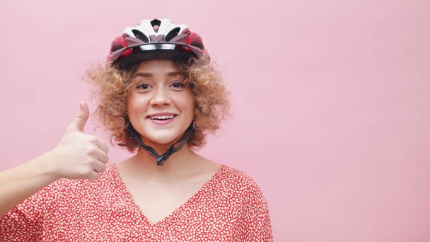 Glückliches junges Mädchen, das einen Fahrradhelm trägt, lächelt und ein Daumen-hoch-Zeichen macht - Foto, Bild