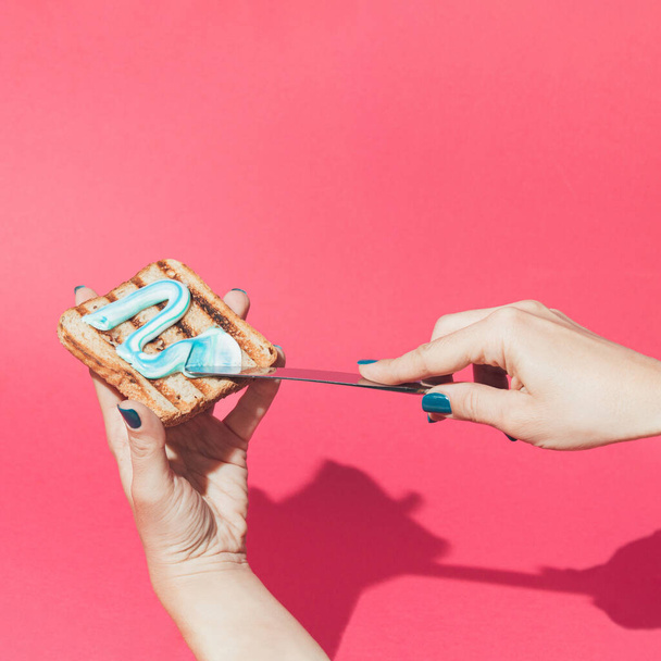 Creative scene of female hands putting a tooth paste on toast bread. Minimal concept. - Fotografie, Obrázek