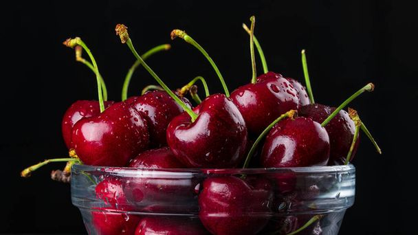 Cherries or Sweet Cherry. Fresh juicy cherries in a glass bowl. Organic farm berries or fruits. High resolution food photo for Grocery store, advertising. Still-life on Black background. - Foto, imagen