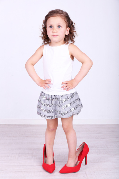 Beautiful small girl in big shoes on wall background - Фото, зображення