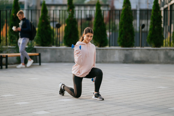 Νεαρό κορίτσι γυμναστικής κάνει ασκήσεις με αλτήρες στο πάρκο της πόλης - Φωτογραφία, εικόνα