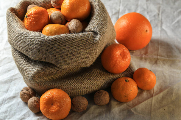 Ripe, tasty and juicy oranges, tangerines in a canvas bag with walnuts on the table. - Foto, afbeelding