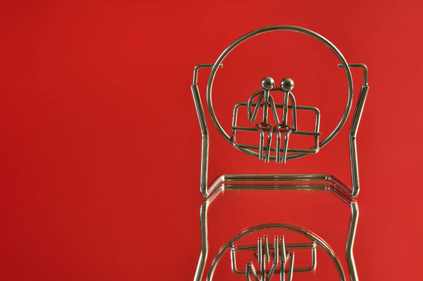 Mooi close-up uitzicht op metalen souvenir van paar zitten op een bank of swing op rode reflecterende achtergrond. Liefde en affectie concept. Kopieerruimte - Foto, afbeelding