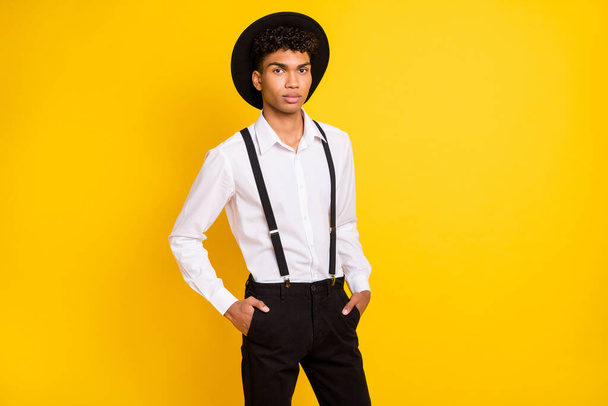 Photo of self-assured cool guy hands pockets wear hat white shirt suspenders isolated yellow color background - Foto, Imagen